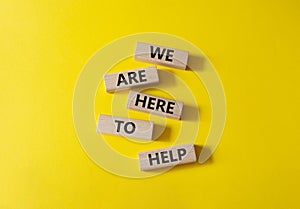 We are here to help symbol. Concept words we are here to help on wooden blocks. Beautiful yellow background. Business and we are