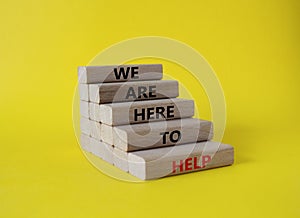 We are here to help symbol. Concept words we are here to help on wooden blocks. Beautiful yellow background. Business and we are