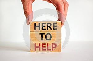 Here to help symbol. Male hand builds stack from blocks with words `here to help`. White table. Beautiful white background. Copy