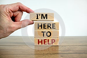 Here to help symbol. Male hand builds stack from blocks with words `i am here to help`. Wooden table. Beautiful white background