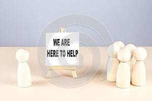 WE ARE HERE TO HELP text on easel with wooden figure, meeting concept