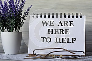 WE ARE HERE TO HELP - words in a notebook on a light background with glasses and a bouquet of lavender