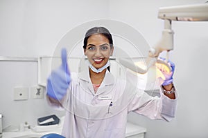 Here to help you maintain good oral health. Portrait of a young female dentist showing thumbs up in her office.