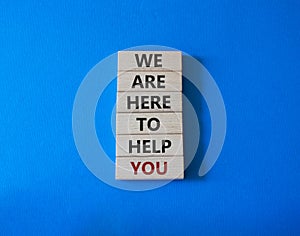 We are here to help you symbol. Concept words we are here to help you on wooden blocks. Beautiful blue background. Business and we