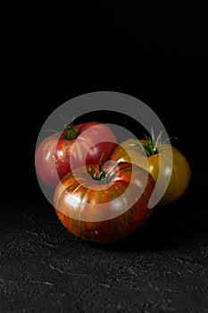 Hereditary tomatoes. Three tomatoes of different colors on a black textured background close-up