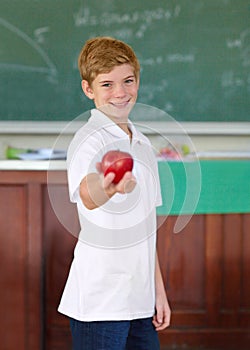 Heres an apple for you. Cute young schoolboy holding an apple in the classroom.