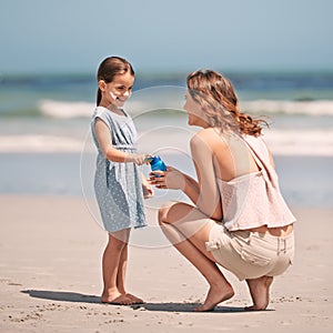 Heres some ocean lotion. a young mother giving her daughter some suntan lotion at the beach.