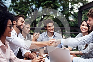 Heres to new business partners. two handsome young businessmen shaking hands while sitting with their colleagues