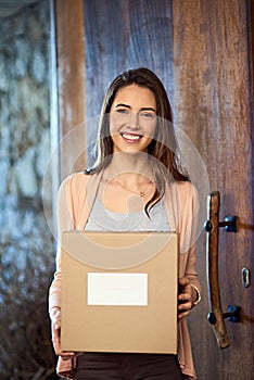 Heres to a new start. Portrait of a smiling young woman carrying a box while moving into her new house.