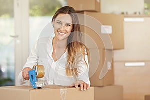 Heres to a new start. Portrait of a smiling young woman packing boxes on moving day.