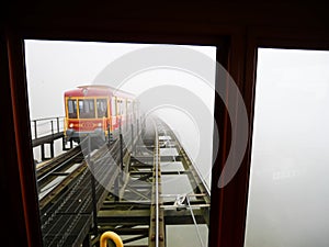 Heritage tram train on lifted aerial electric light rail transit covered in foggy misty winter weather, scenic mountain landscape