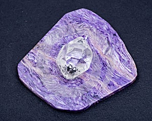 Herkimer Diamond placed on top grade Charoite polished slab from Sakha Republic, Siberia, Russia. On black background.