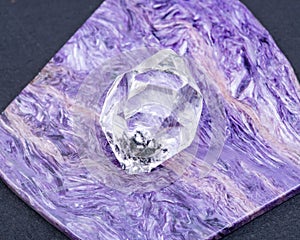 Herkimer Diamond placed on top grade Charoite polished slab from Sakha Republic, Siberia, Russia. On black background.