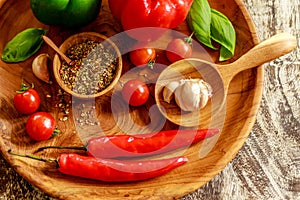 ÃÂ¡herry tomatoes, garlic, chili, basil leaves, red and green capsicums, mix of dry spices in a wooden pot over wooden table