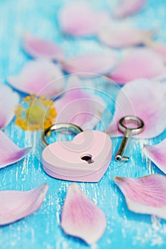 Pink heart padlock with petals on wooden backrgound