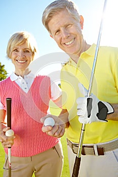 Hes been an avid golfer for years. Elderly couple holding their golf clubs and balls on the green.