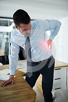Hes been sitting for too long. a young businessman experiencing back pain highlighted in glowing red at work.