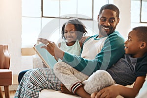 Hes the best story teller. a father and his children reading a book indoors.