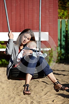 Hes a big responsibility. Young mom on a park swing with her baby boy.