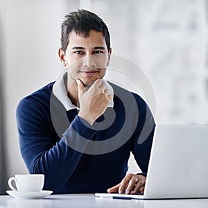 Hes confident in his ability to succeed. Portrait of a young businessman using a laptop while sitting at a desk in an