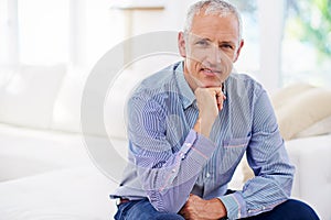 Hes confident and mature. Portrait of a smiling mature man sitting on a sofa in his living room.