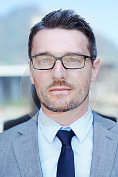 Hes the consummate professional. Head and shoulders portrait of a serious-looking businessman standing outside.