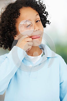 Hes a curious mind. Portrait of a cute young boy looking while holding a magnifying glass over his closed eye.