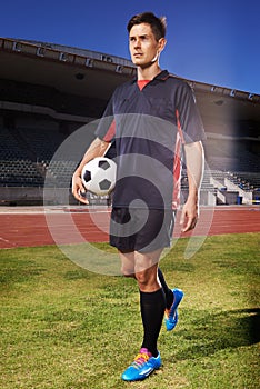 Hes dedicated to his sport. a young footballer standing on a field holding a ball.