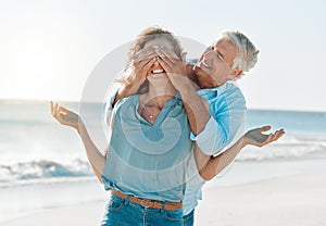 Hes full of surprises. a man covering his wifes eyes while on the beach.