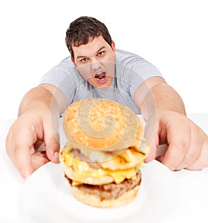 Hes going to destroy that burger. An obese young man reaching out to grab a huge hamburger and looking ravenous.