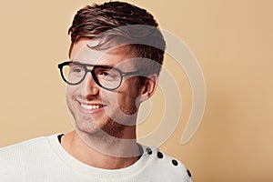 Hes got a carefree outlook on life.... Studio headshot of a stylishly-dressed young man smiling and wearing glasses.