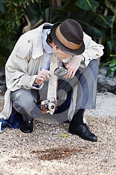 Hes got a keen investigative eye. Curious private investigator looking through a magnifying glass at the ground for