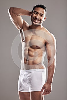 Hes got the ladies swooning. Studio portrait of a muscular young man posing against a grey background.