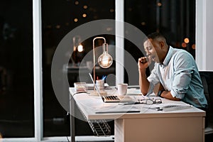 Hes had a long night at the office. Shot of a handsome young businessman yawning and feeling tired while working late in