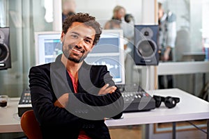 Hes made a name for himself in the biz. A handsome music producer sitting with arms folded in his studio.