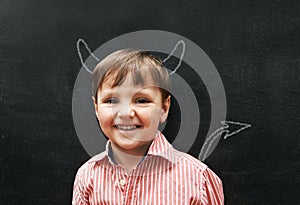 Hes a mischievous little one. Stuido portrait of a young boy with chalk-drawing horns and tail behind him.