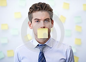 Hes not allowed to disclose company secrets. Portrait of a young office worker with a sticky note stuck over his mouth.