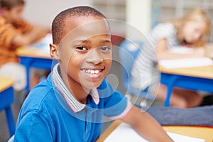 Hes proud of his school and education. Happy young african-american school pupil smiling up at the camera in class -