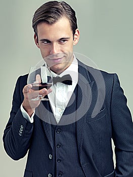 Hes on the prowl. A studio shot of a dapper young man holding a glass of red wine and looking mischievous.