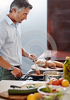 Hes quite the chef. a handsome mature man cooking dinner in his kitchen at home.