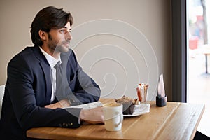 Hes a regular here. A thoughtful businessman sitting in a coffee shop and looking out of the window.