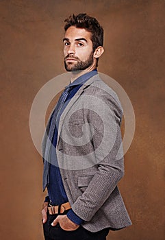 Hes a snappy dresser. a stylishly dressed young man posing against a brown background.