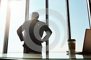 Hes soaring high in the corporate world. Rearview shot of a young businessman looking out the window in an office.