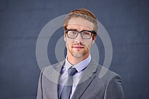 Hes stylish and successful. Portrait of a handsome young businessman standing against a gray background.