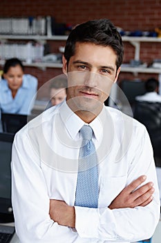 Hes sure of his business skill. A handsome young businessman crossing his arms confidently in the office.