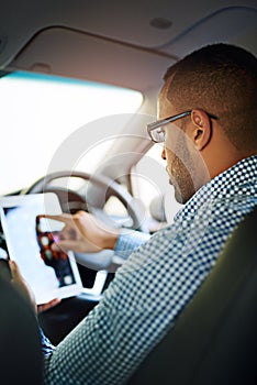 Hes too busy browsing to be bothered by the road. a young businessman using a digital tablet while driving a car.