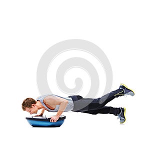 Hes working to acheive a muscular body. A handsome young man using a bosu-ball for an upper body workout. photo