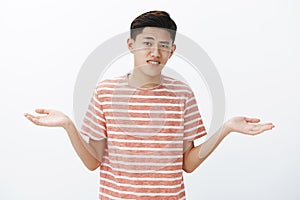 Hesitant attractive young asian guy with dark hair shrugging spreading hands sideways as making hard choice or decision