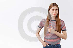 Hesitant and suspicious, unsure young fair-haired woman in striped t-shirt, frowning, squinting uncertain, pointing left