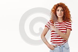 Hesitant timid uncertain young cute redhead curly woman hard taking decision pointing left frowning doubtful smirking